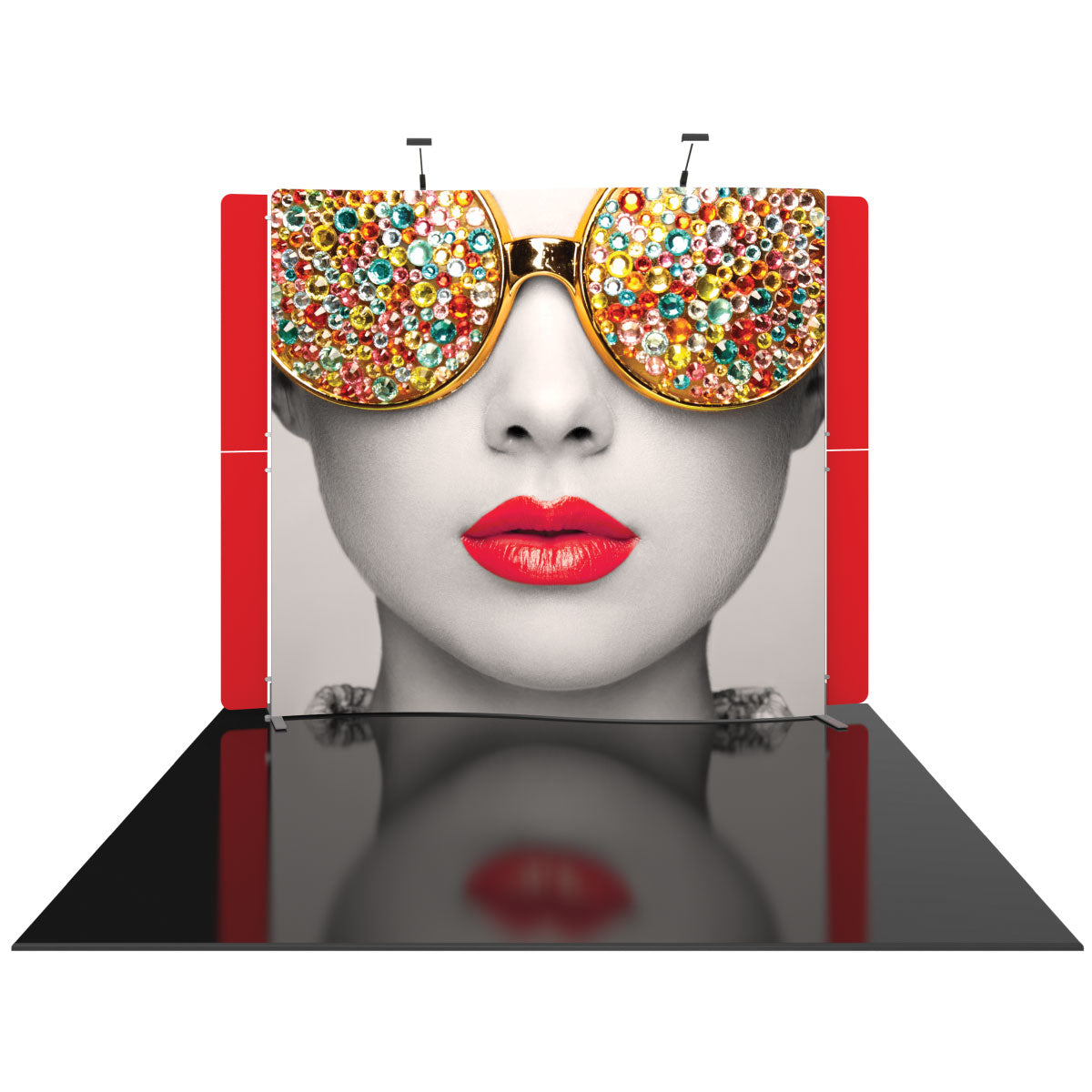 Trade show display with a large printed backdrop featuring a close-up face wearing gem-studded sunglasses and bold lips