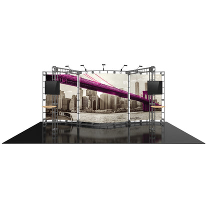 Trade show display featuring curved truss frame with large cityscape backdrop, mounted screens, and spotlighting