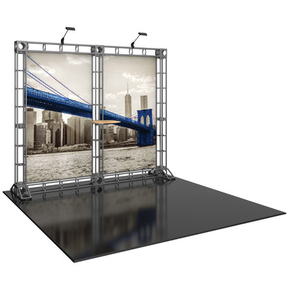 Trade show display featuring a truss frame with backlit cityscape panels and a center shelf
