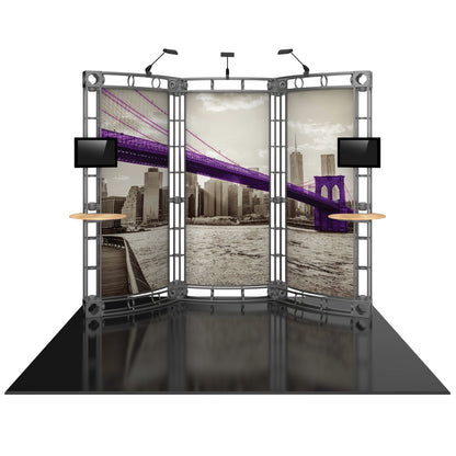 Trade show truss display featuring curved panels with city skyline graphics, mounted monitors, and small shelves