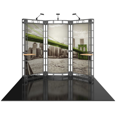 Three-panel modular truss display with scenic city bridge graphic, spotlight fixtures, and tabletop shelves for trade shows