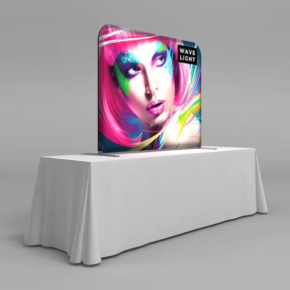 Backlit tabletop trade show display featuring vibrant face art on a fabric graphic frame on an event table