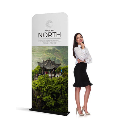 Tall trade show banner stand featuring travel tour advertisement with Asian pavilion and landscape, next to smiling businesswoman